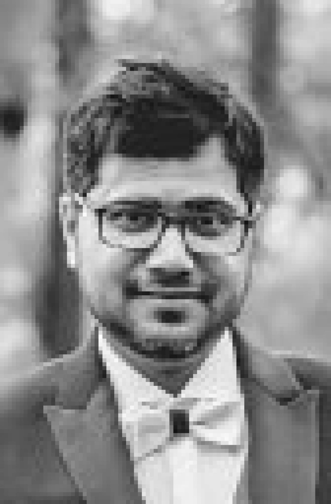 Mężczyzna w eleganckim garniturze z okularami, uśmiechający się w plenerze.