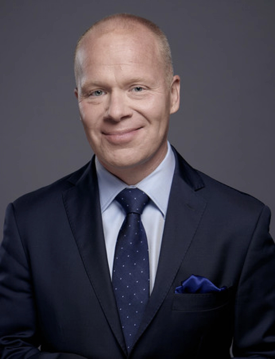 Mężczyzna w garniturze z uśmiechem, pozujący na tle jednolitego koloru.