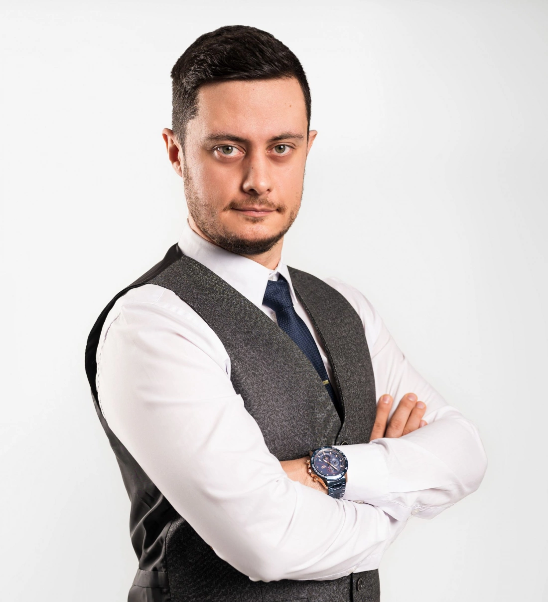 Mężczyzna w eleganckim stroju, z założonymi rękami, na białym tle.
