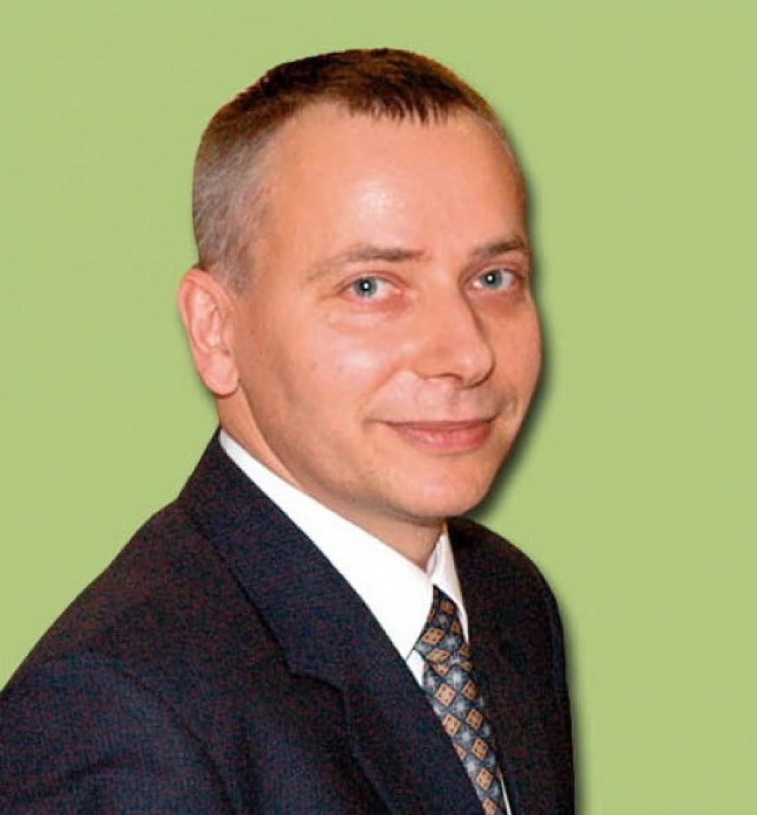 Mężczyzna w garniturze, uśmiechający się na zielonym tle.