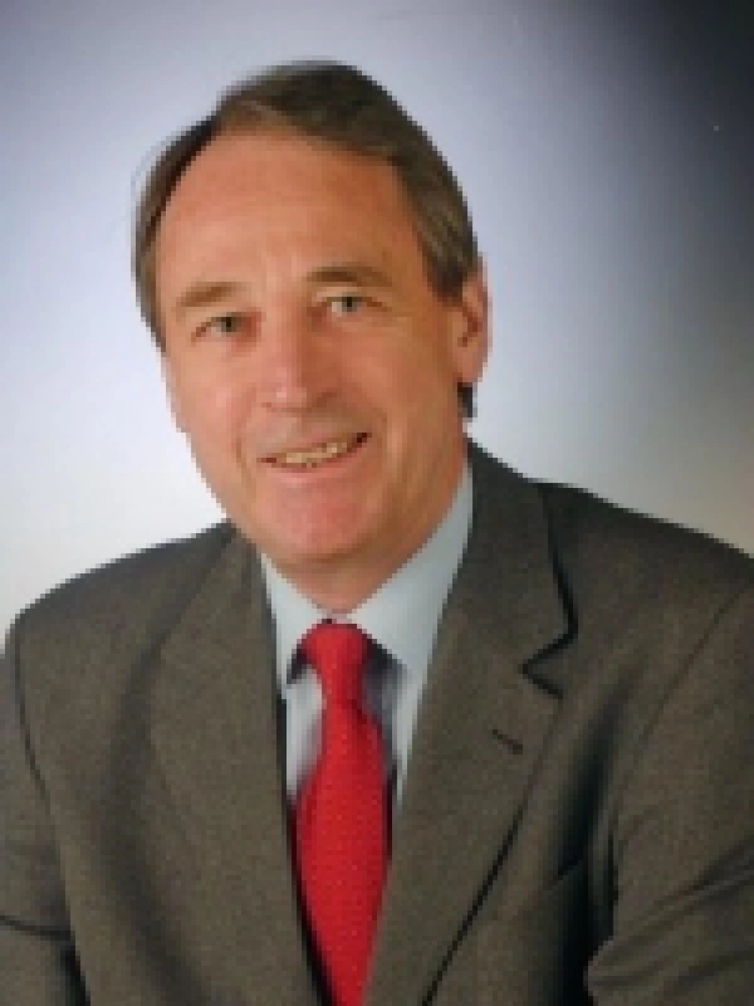 Mężczyzna w garniturze z uśmiechem, na neutralnym tle.