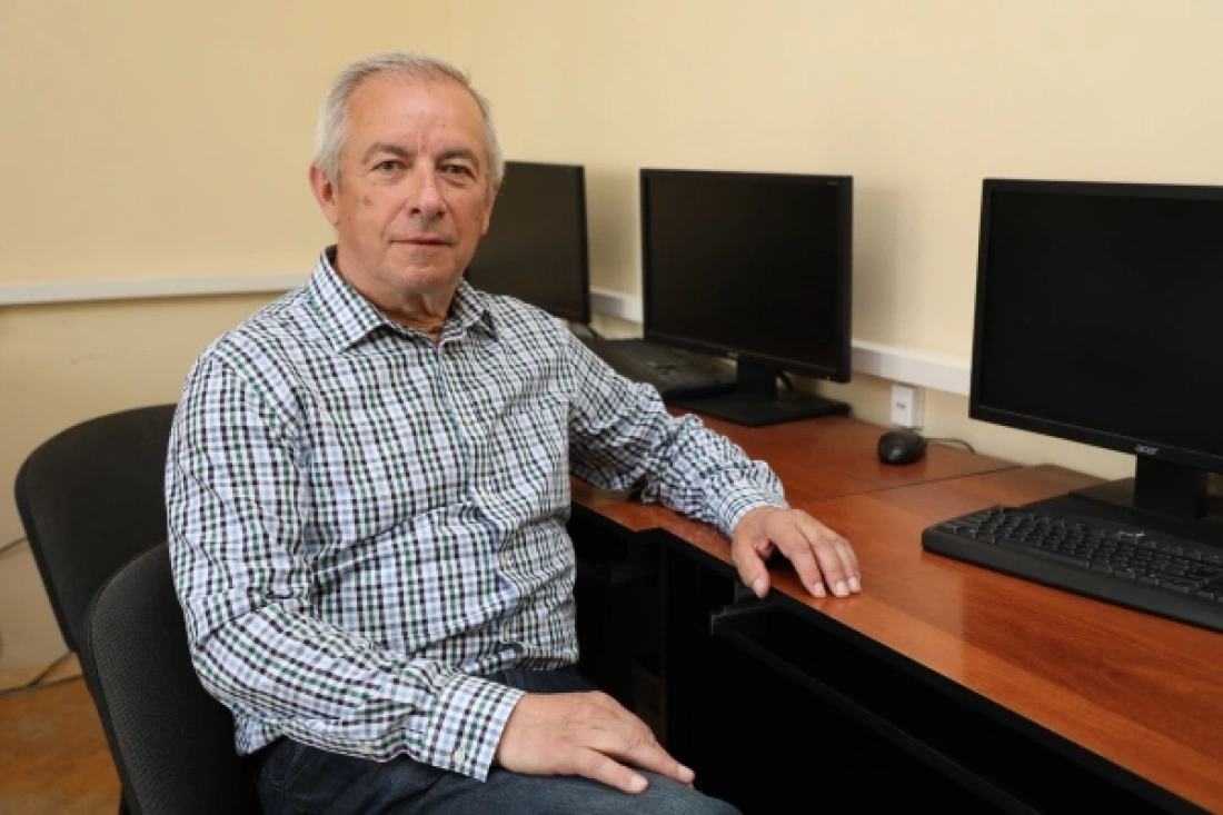 Mężczyzna w koszuli w kratę siedzi przy biurku z komputerami.