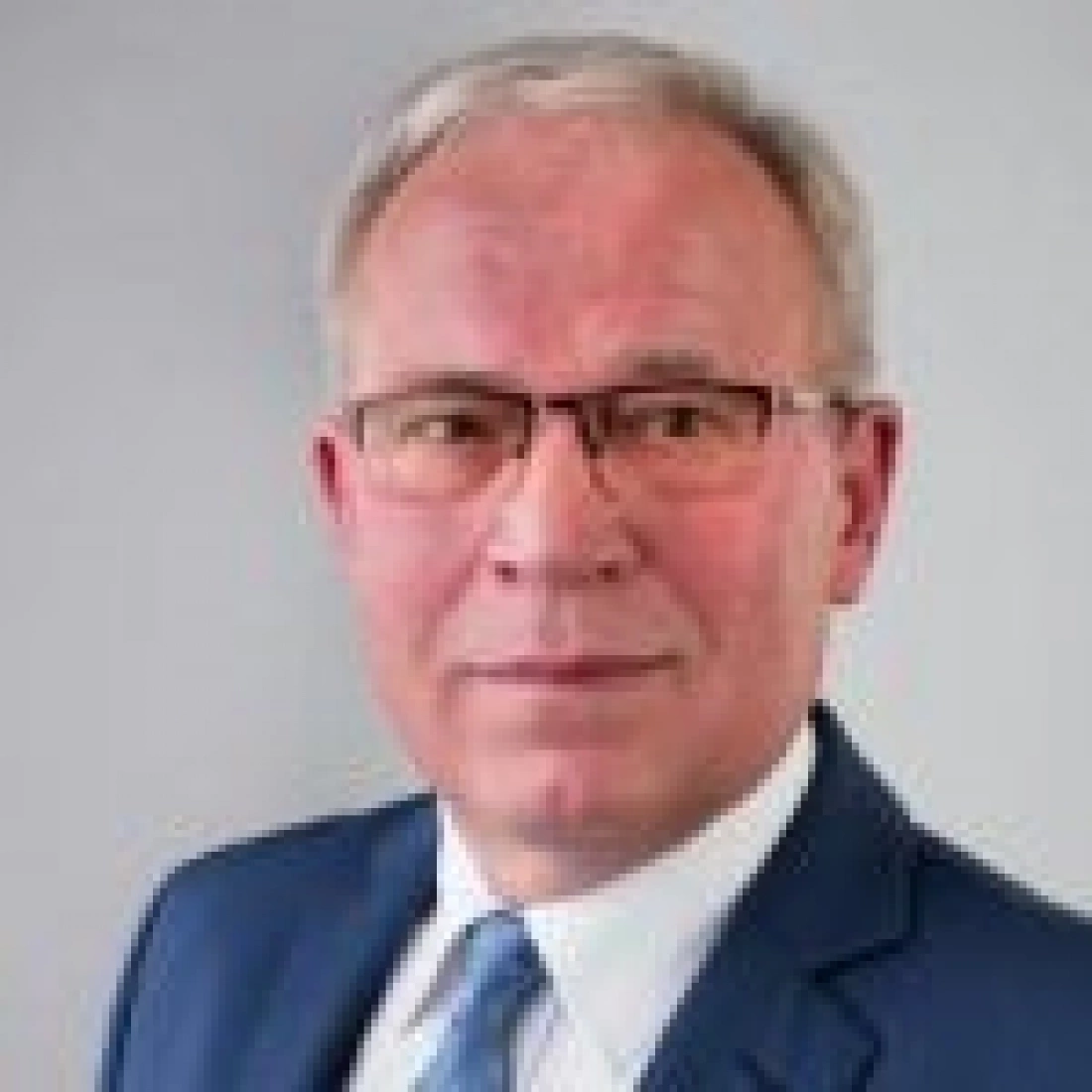 Mężczyzna w garniturze z okularami, patrzący w kamerę.