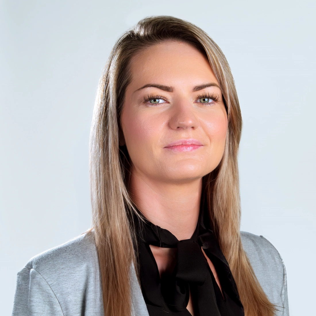 Portret kobiety o długich włosach, ubranej w elegancki strój, na tle jasnej ściany.