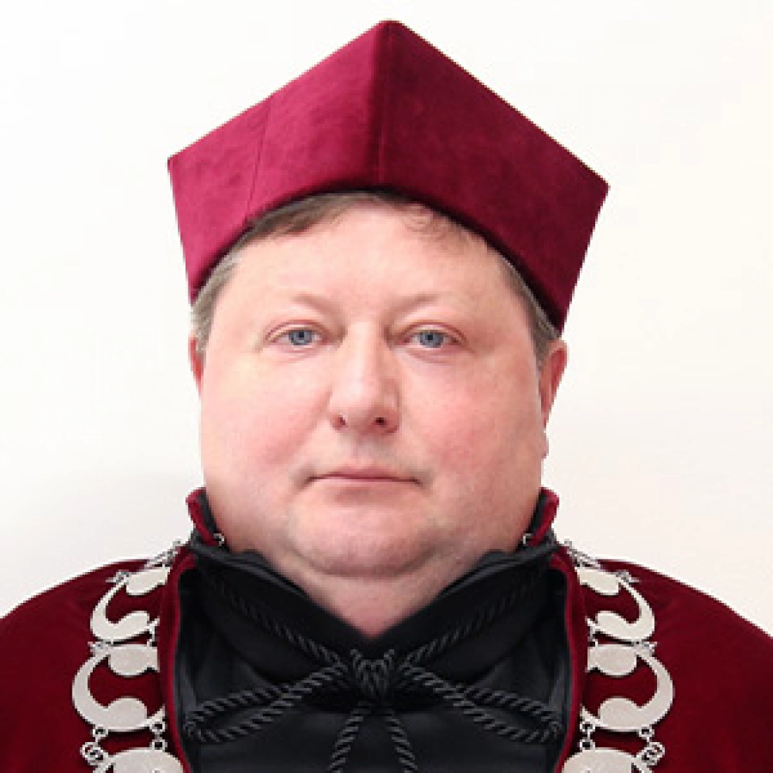 Mężczyzna w szkarłatnym stroju akademickim z nakryciem głowy.