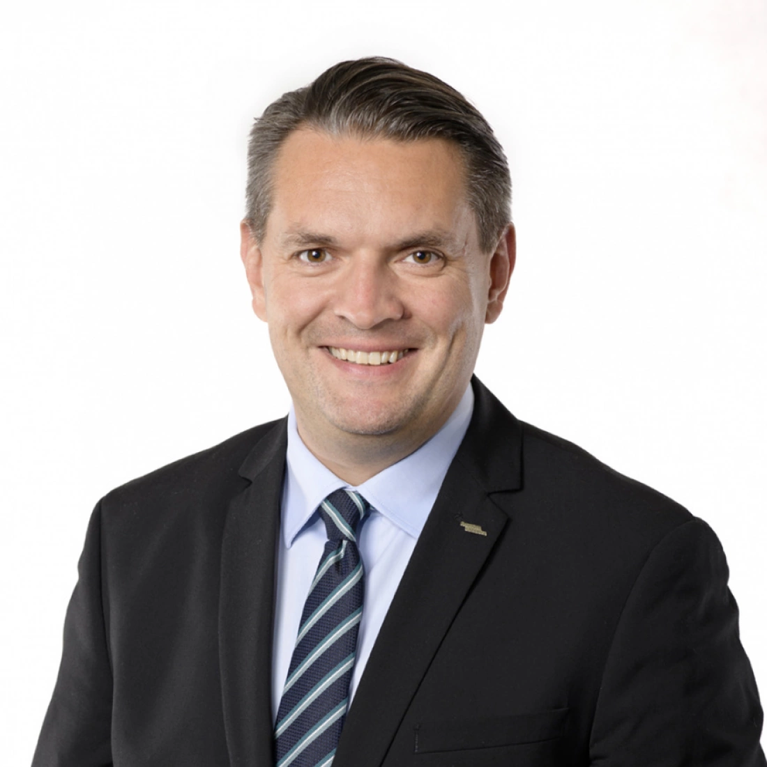 Mężczyzna w ciemnym garniturze uśmiecha się do kamery.