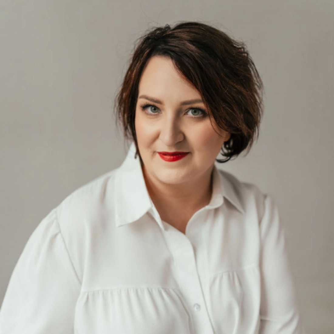 Portret kobiety w białej koszuli, z krótkimi, ciemnymi włosami i wyrazistym makijażem.