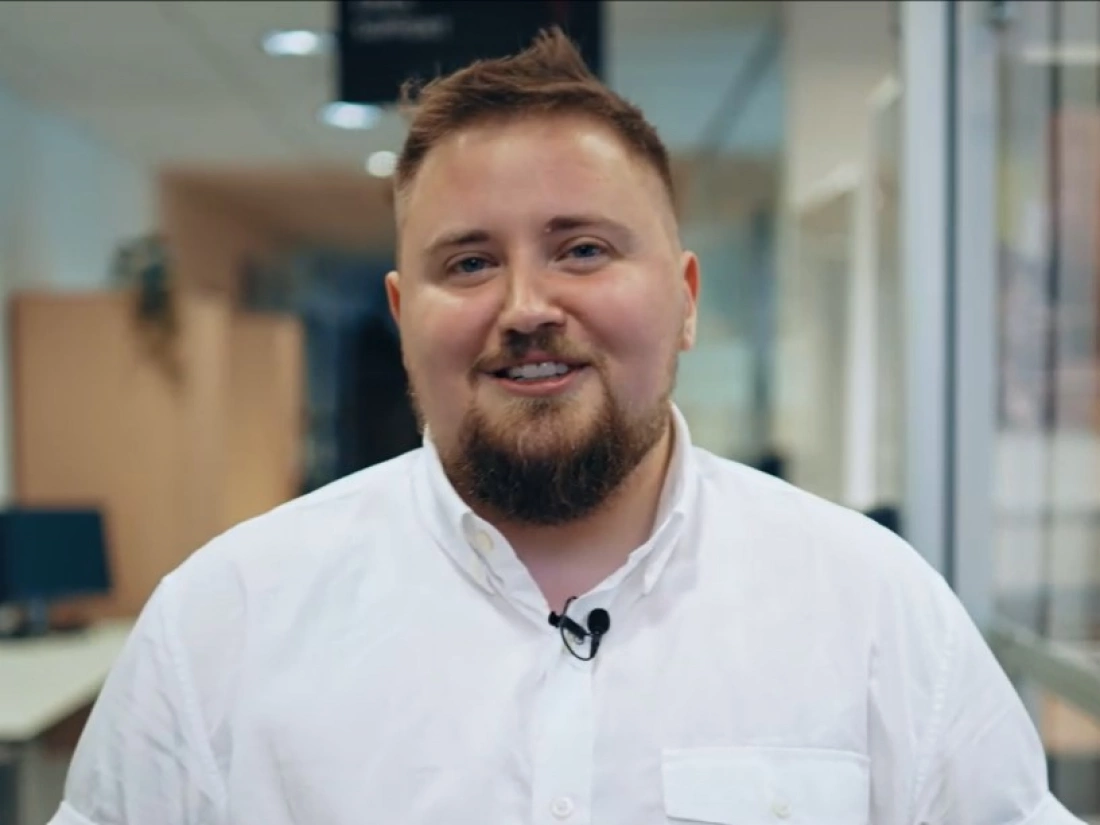 Mężczyzna w białej koszuli uśmiecha się, stojąc w biurze.