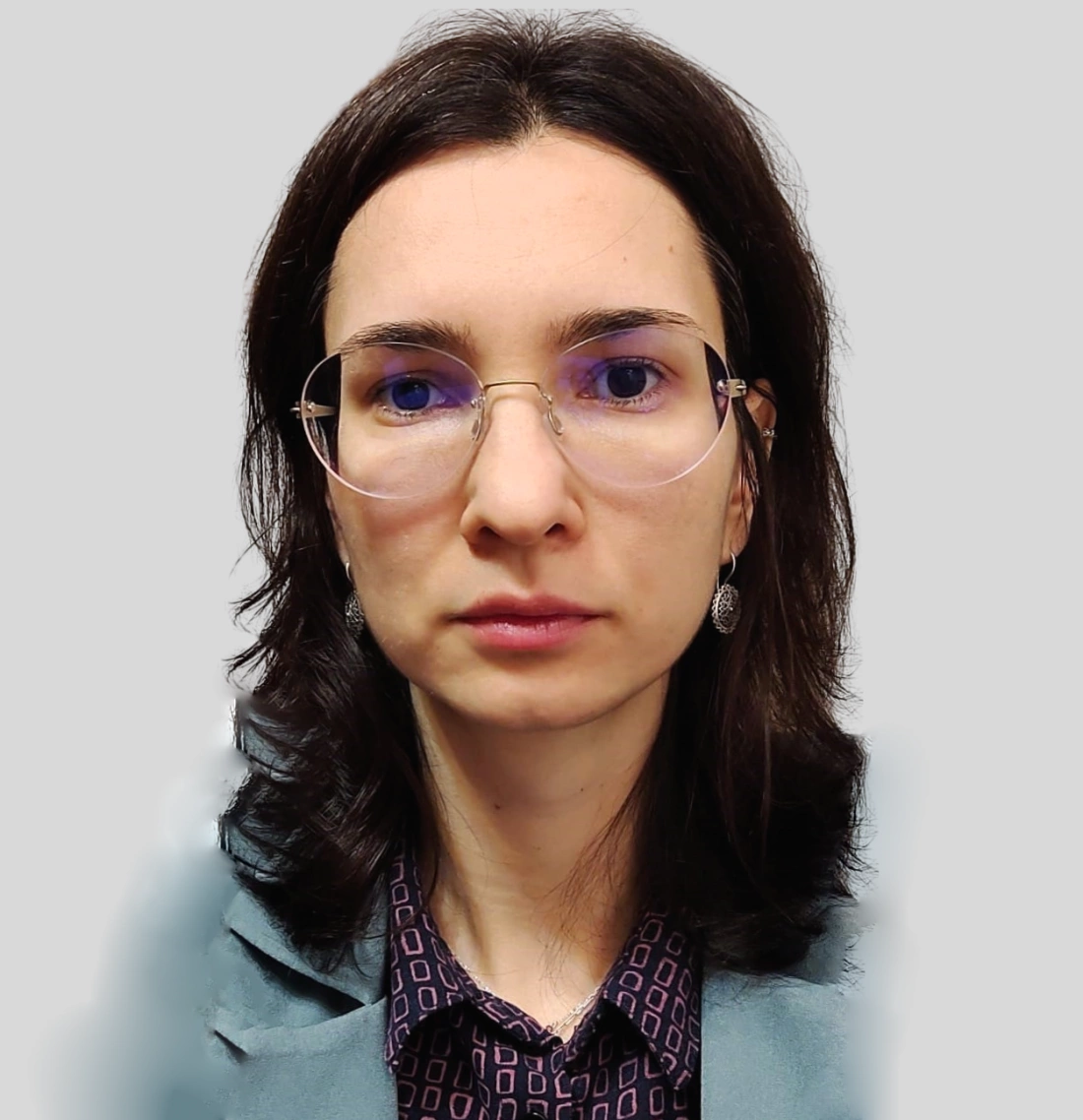 Portret kobiety o długich ciemnych włosach, w okularach, z neutralnym wyrazem twarzy.