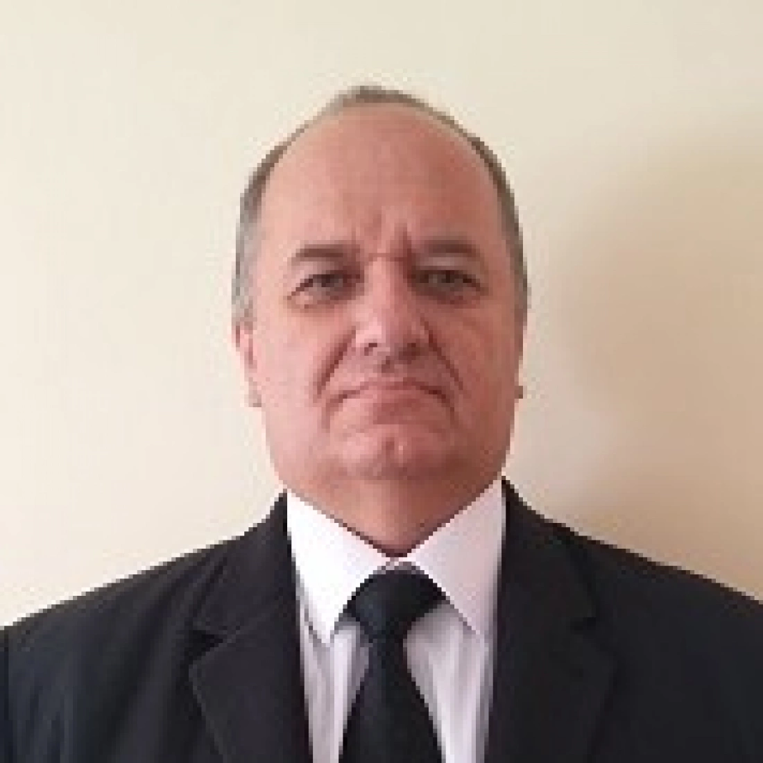 Mężczyzna w garniturze i krawacie, stojący na tle jasnej ściany.