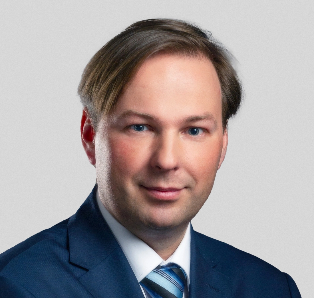 Mężczyzna w garniturze, z krótkimi włosami i niebieskimi oczami, na neutralnym tle.