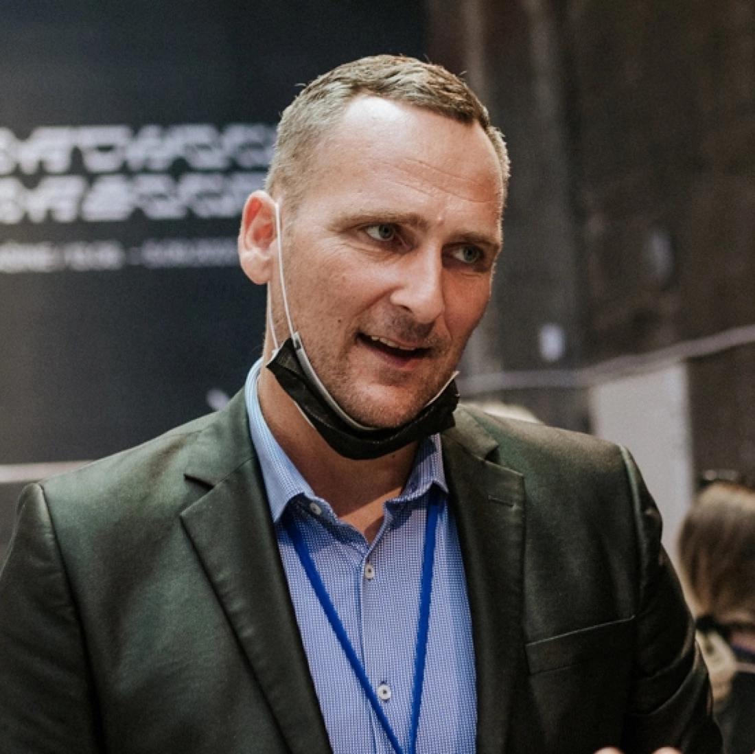 Mężczyzna w garniturze rozmawia, nosząc maseczkę ochronną.