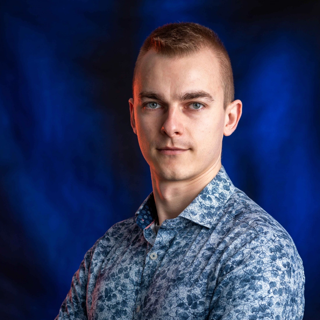 Mężczyzna w kwiatowej koszuli stoi na tle w odcieniach niebieskiego.