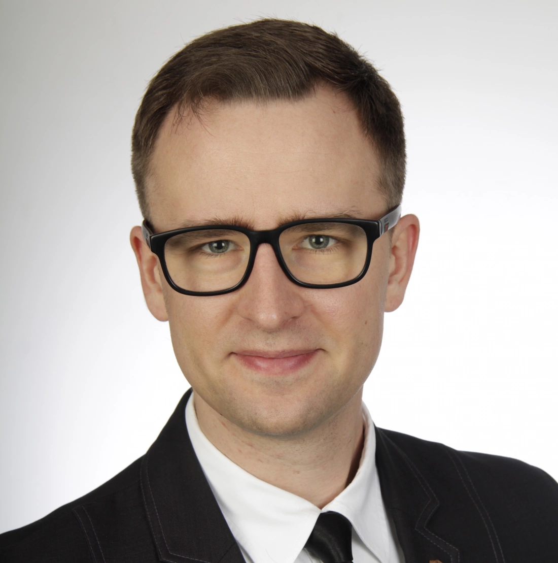 Mężczyzna w okularach, uśmiechnięty, ubrany w elegancki garnitur z krawatem.