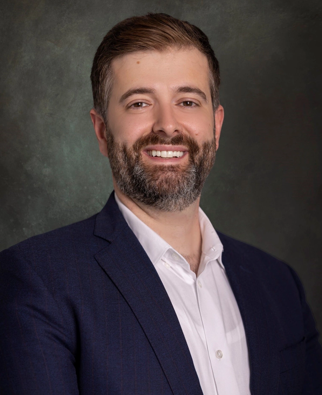 Mężczyzna w garniturze, uśmiechający się na tle w jednolitym kolorze.