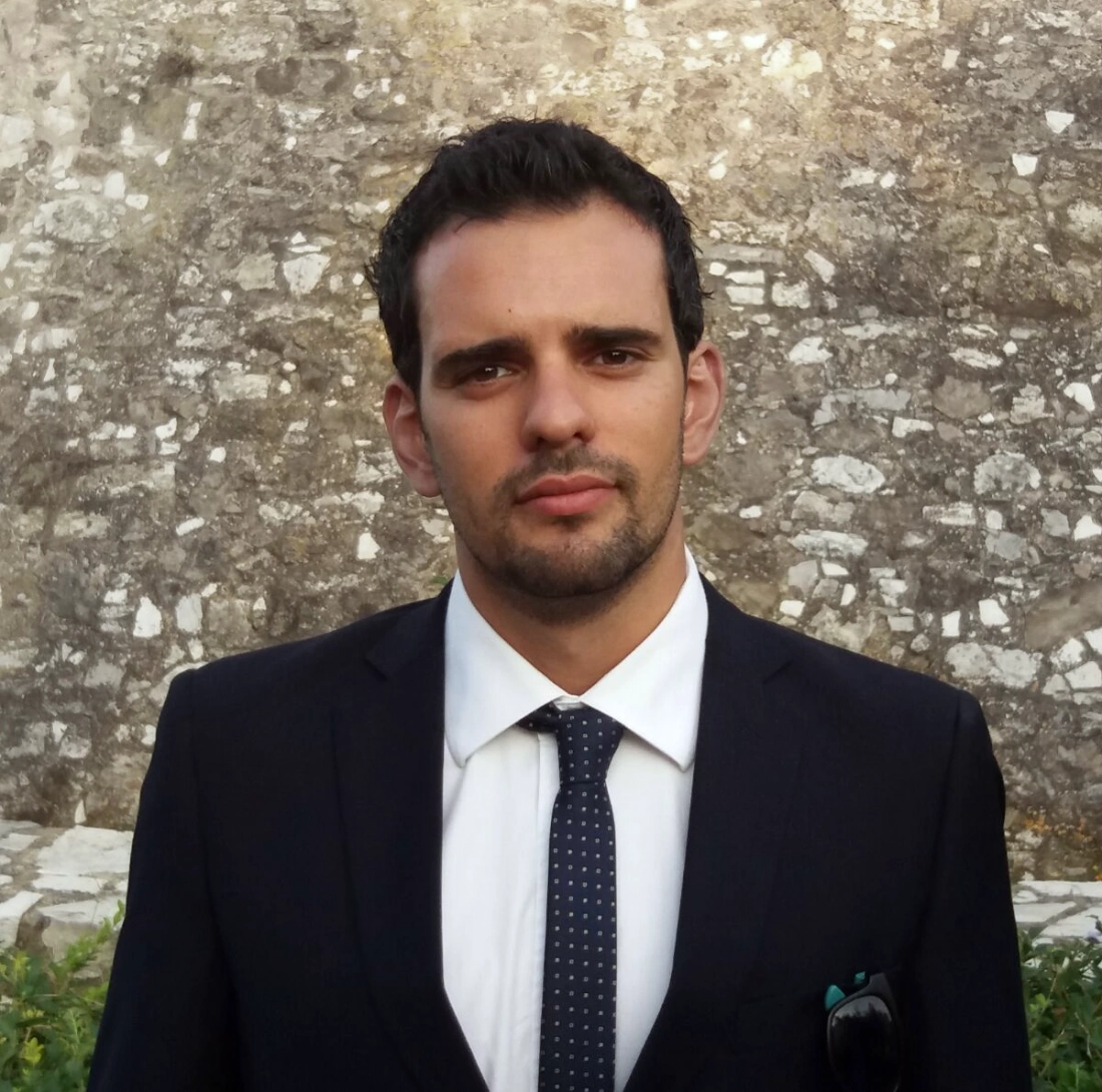 Mężczyzna w eleganckim garniturze stoi przed kamienistą ścianą.