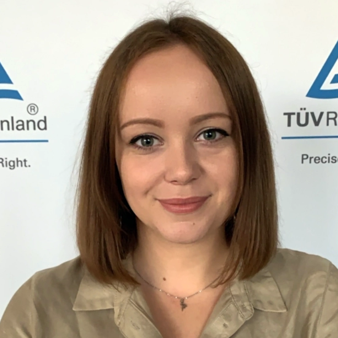 Kobieta z krótkimi, brązowymi włosami, uśmiechająca się na tle logotypu TÜV Rheinland.