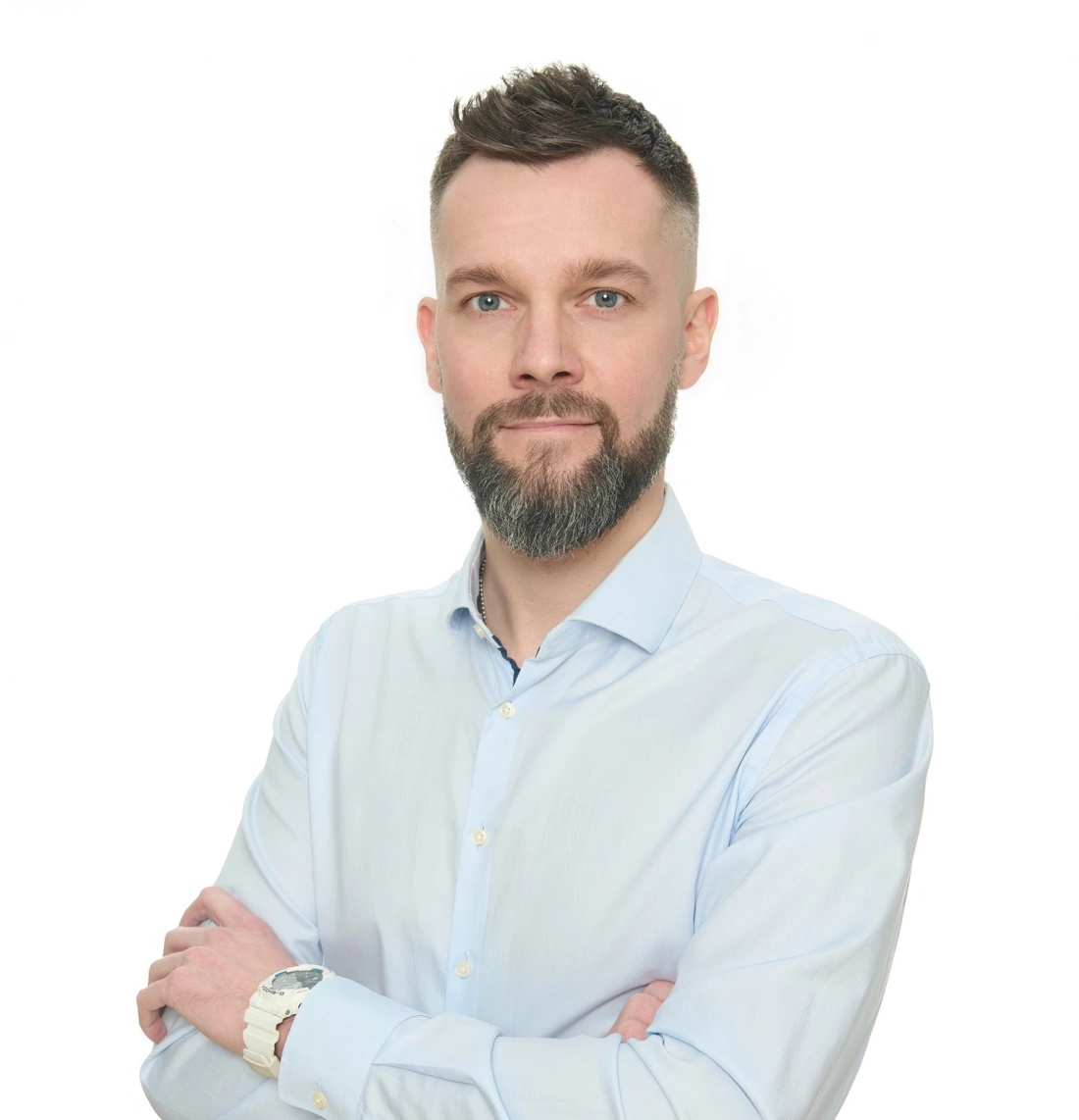 Mężczyzna z brodą w jasnej koszuli, z założonymi rękami, na białym tle.