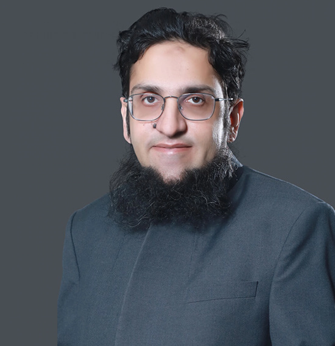 Mężczyzna w okularach i ciemnym garniturze z długą brodą na jednolitym tle.