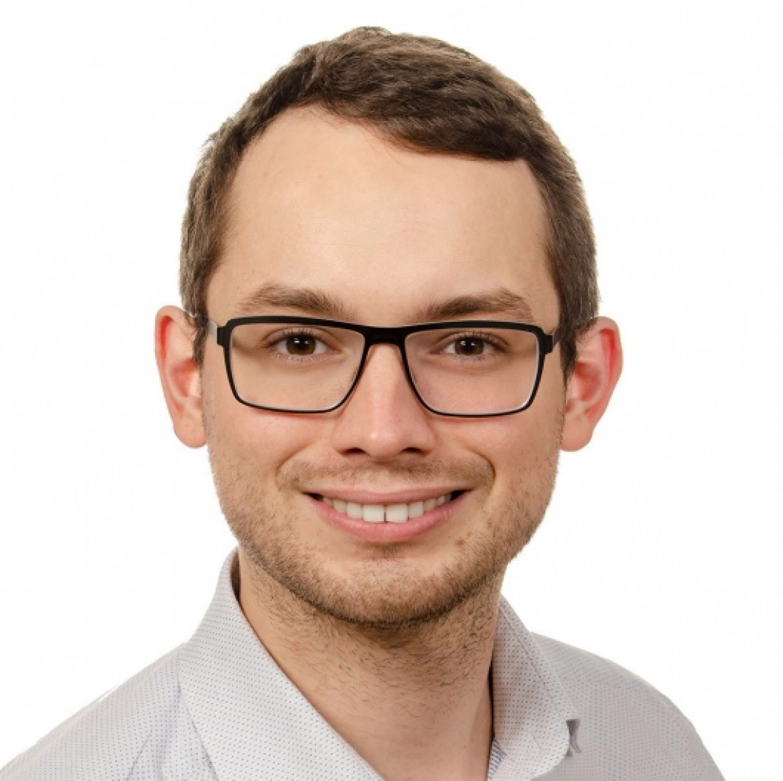 Młody mężczyzna w okularach, uśmiechający się w białej koszuli.