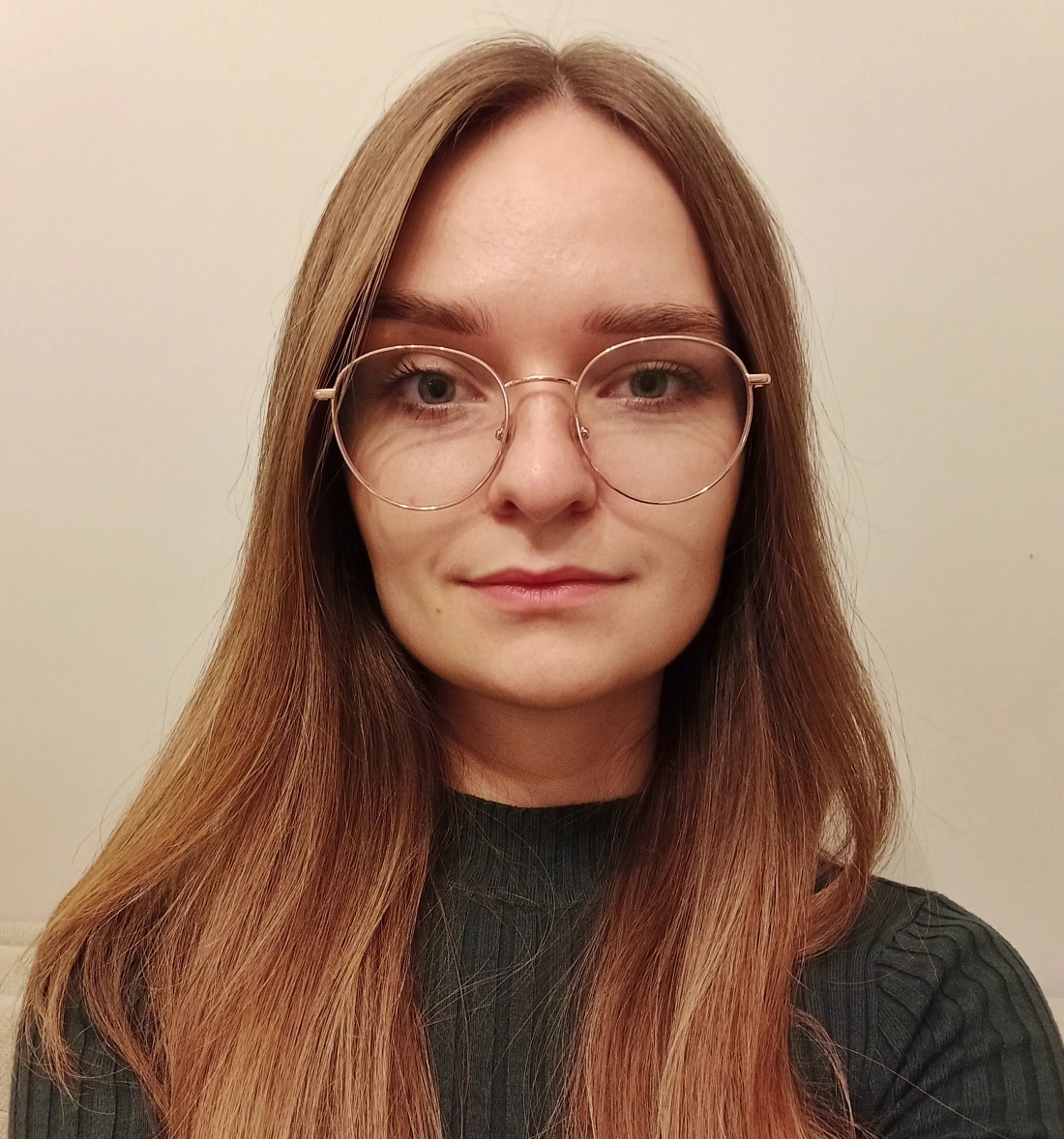 Młoda osoba z długimi włosami, nosząca okulary, patrzy w obiektyw.