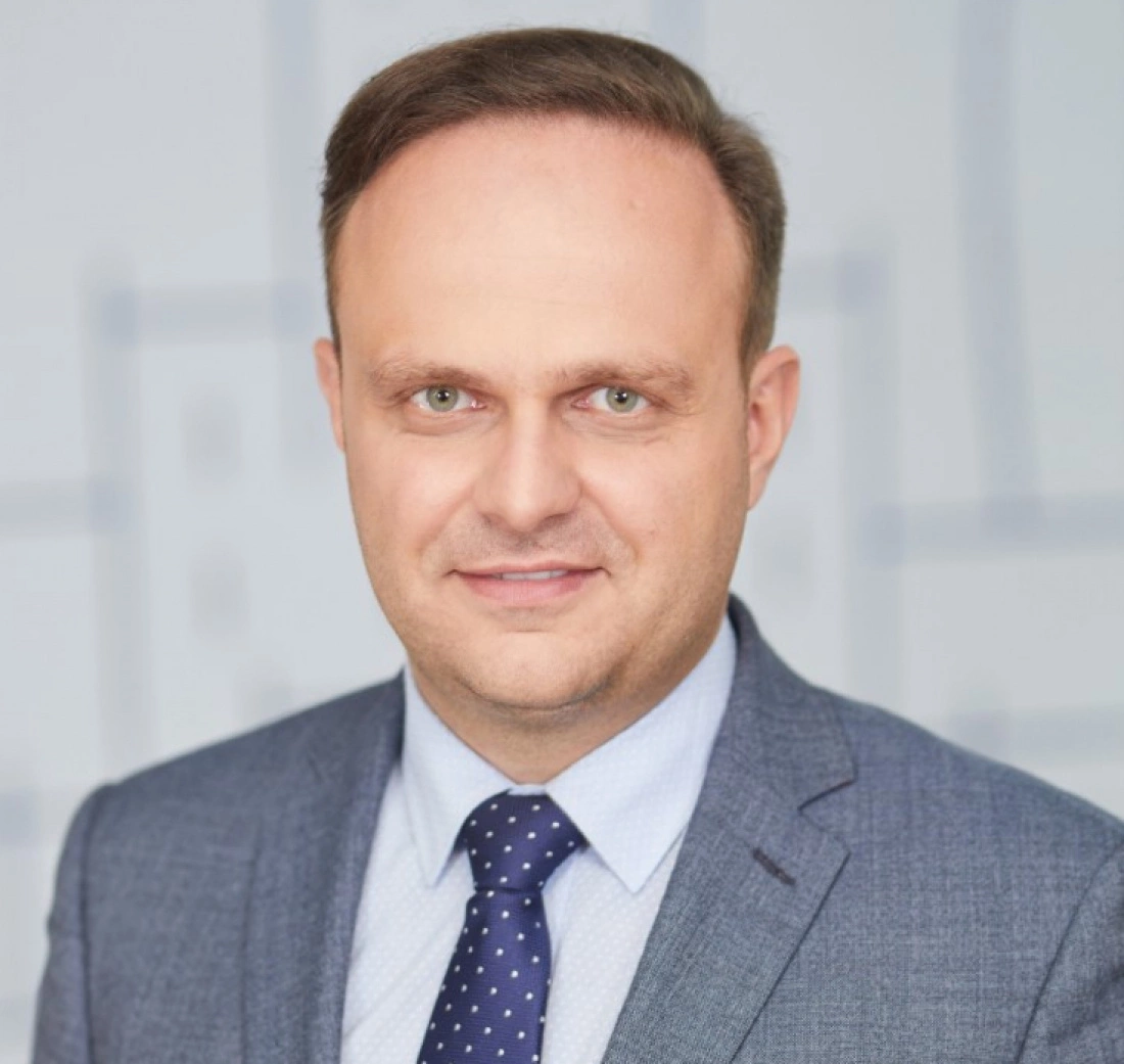 Mężczyzna w eleganckim garniturze na tle neutralnego tła.