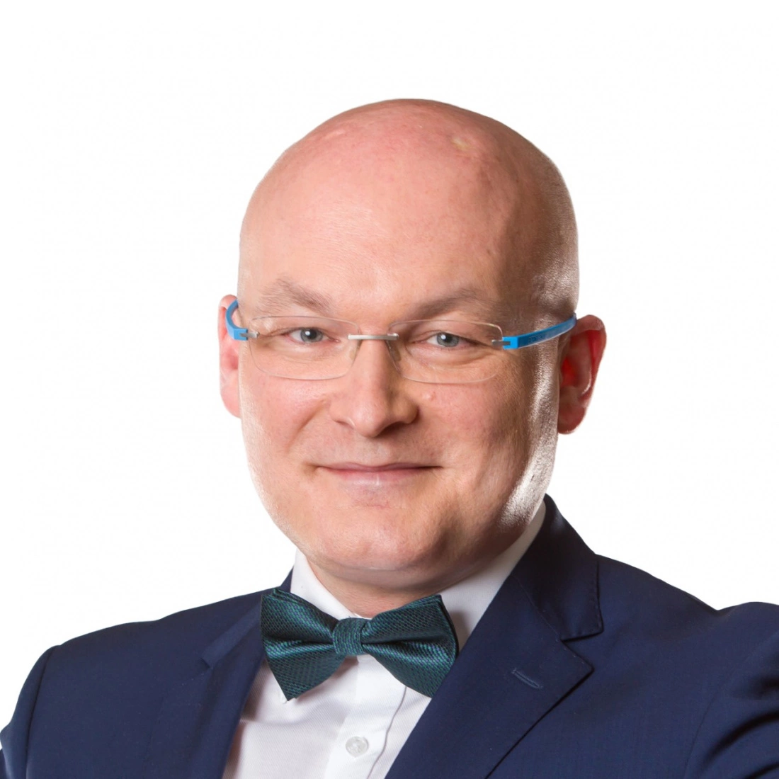 Mężczyzna w garniturze, z długimi okularami i muszką, uśmiechający się.