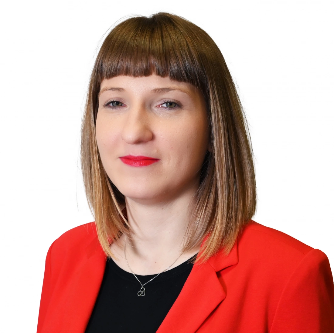 Kobieta w czerwonym żakiecie z prostymi włosami i wyrazistymi ustami na jasnym tle.