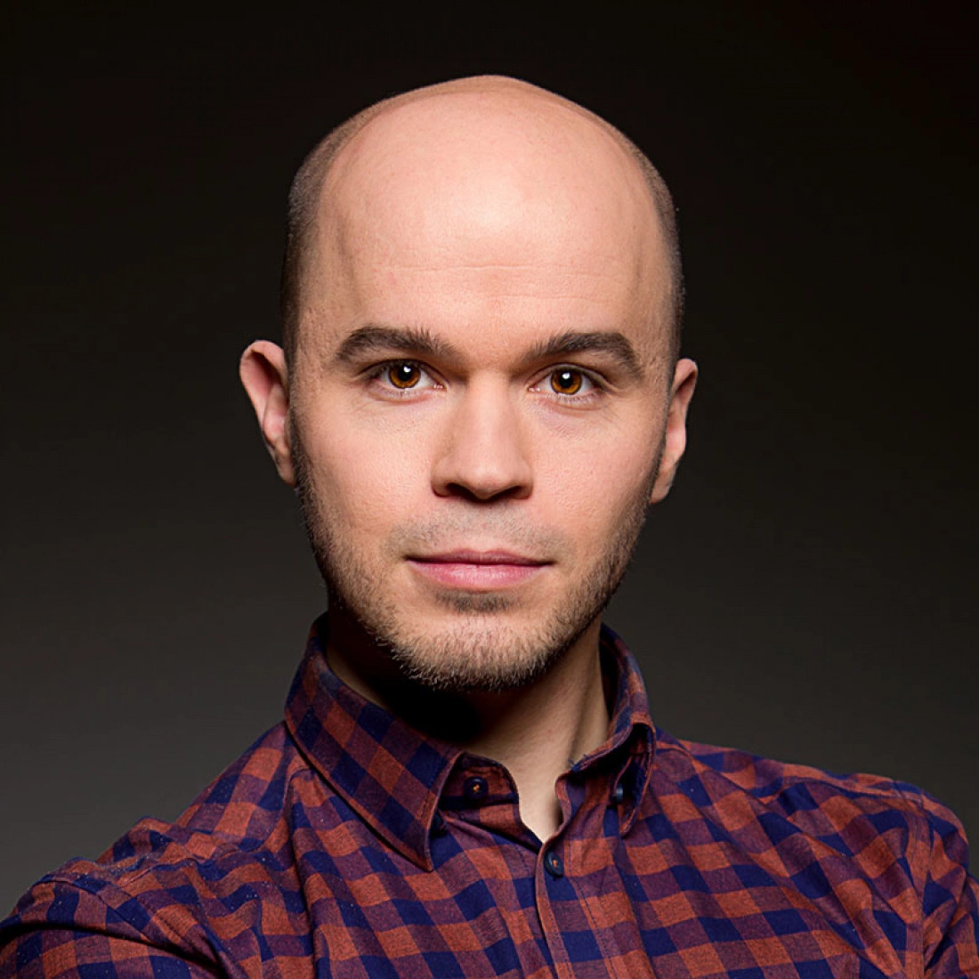 Mężczyzna w koszuli w kratę, z krótkimi włosami, spogląda w kamerę.