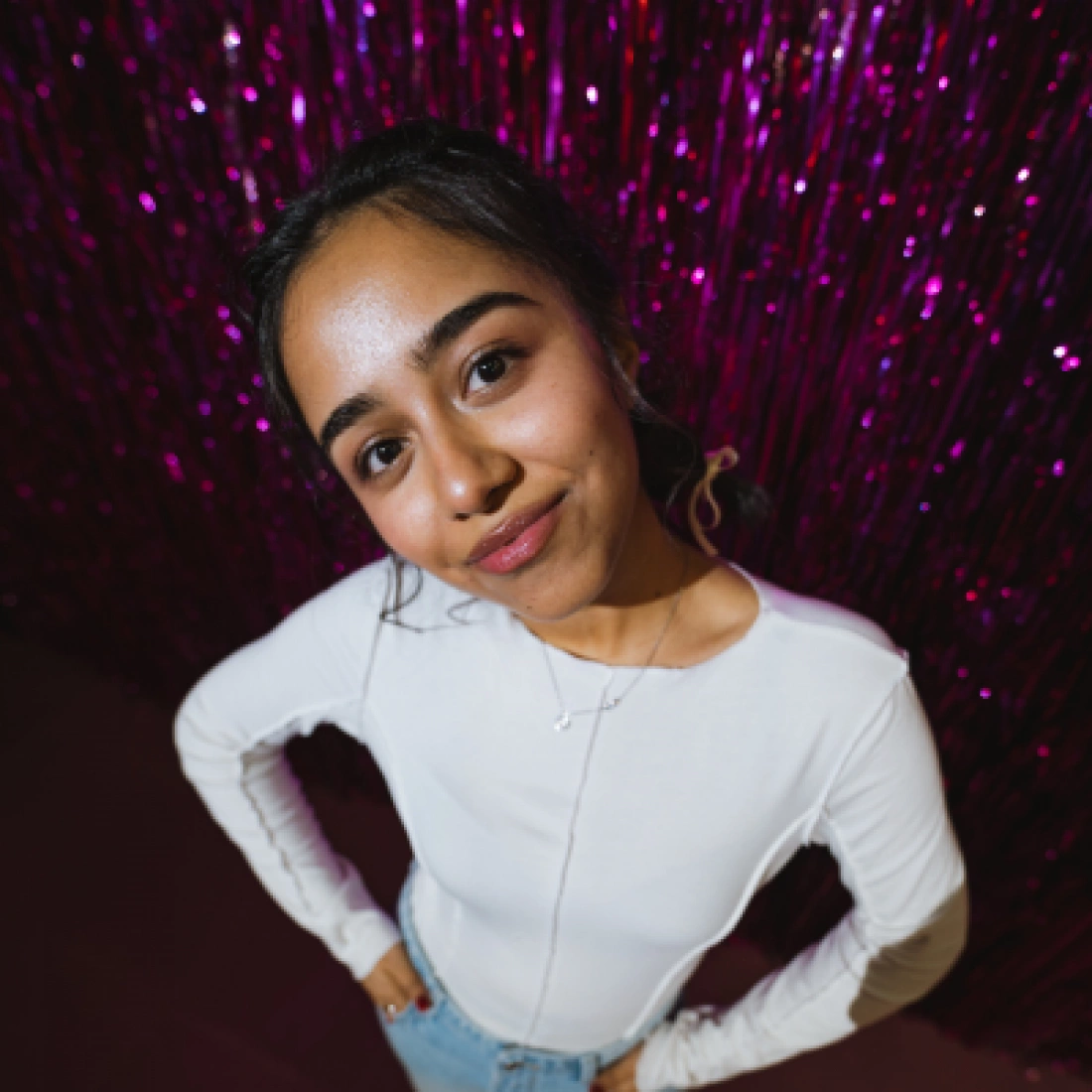 Młoda kobieta w białej bluzce pozująca przed błyszczącym różowym tłem.