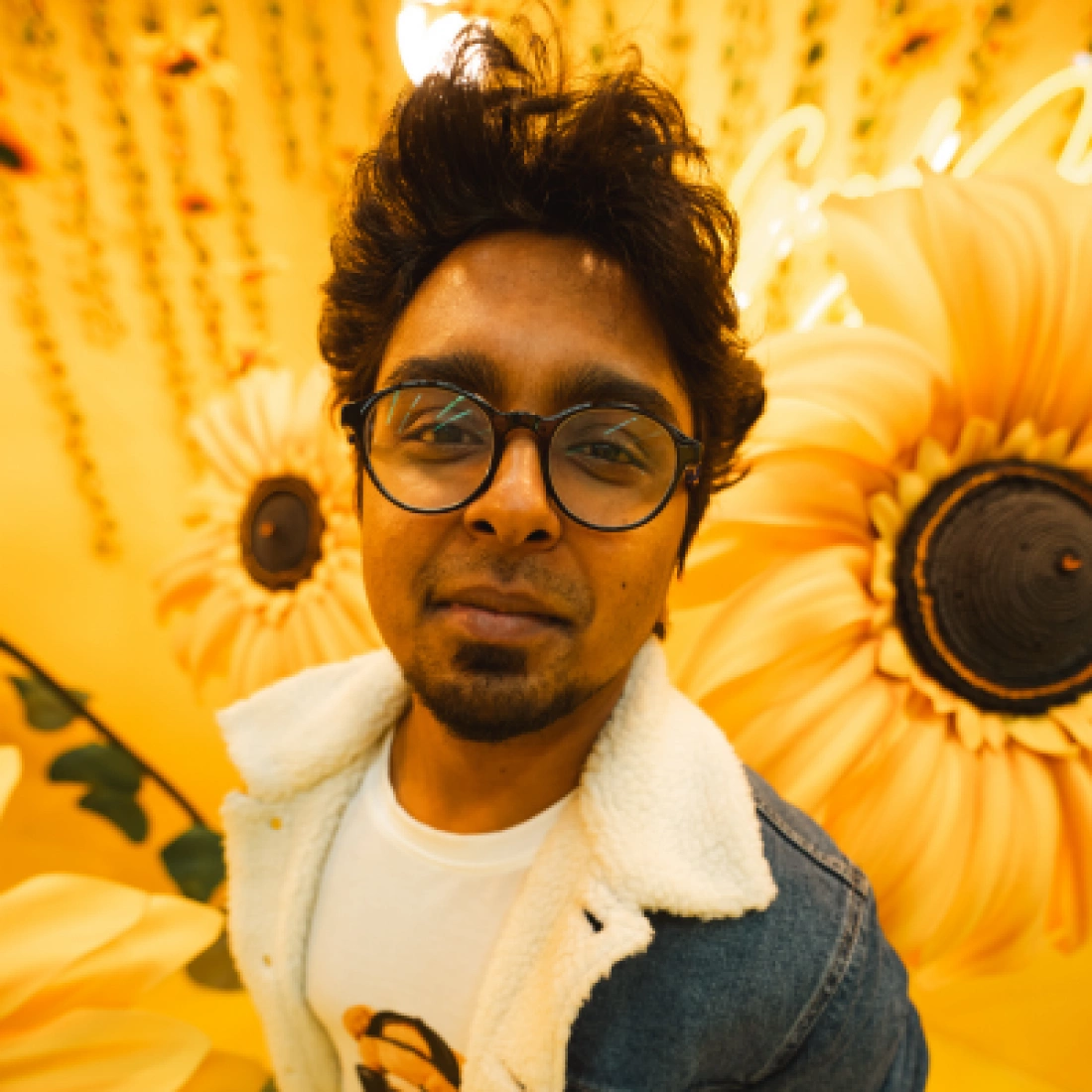 Mężczyzna w okularach pozujący przed tłem z kwiatami słonecznika.