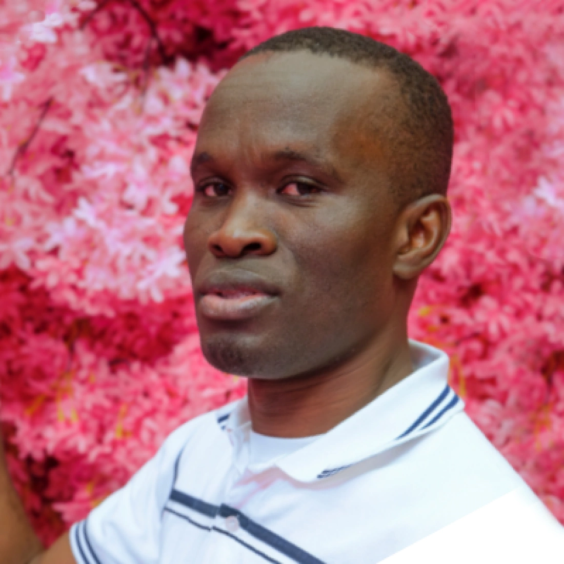 Mężczyzna w białej koszulce stoi przed różowym tłem kwiatów.