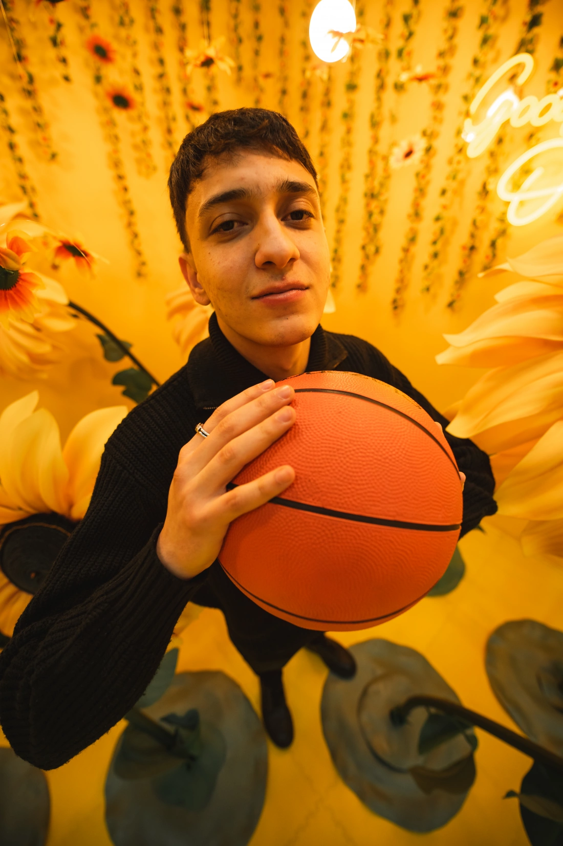 Młody mężczyzna trzyma piłkę do koszykówki wśród kwiatów na żółtym tle.