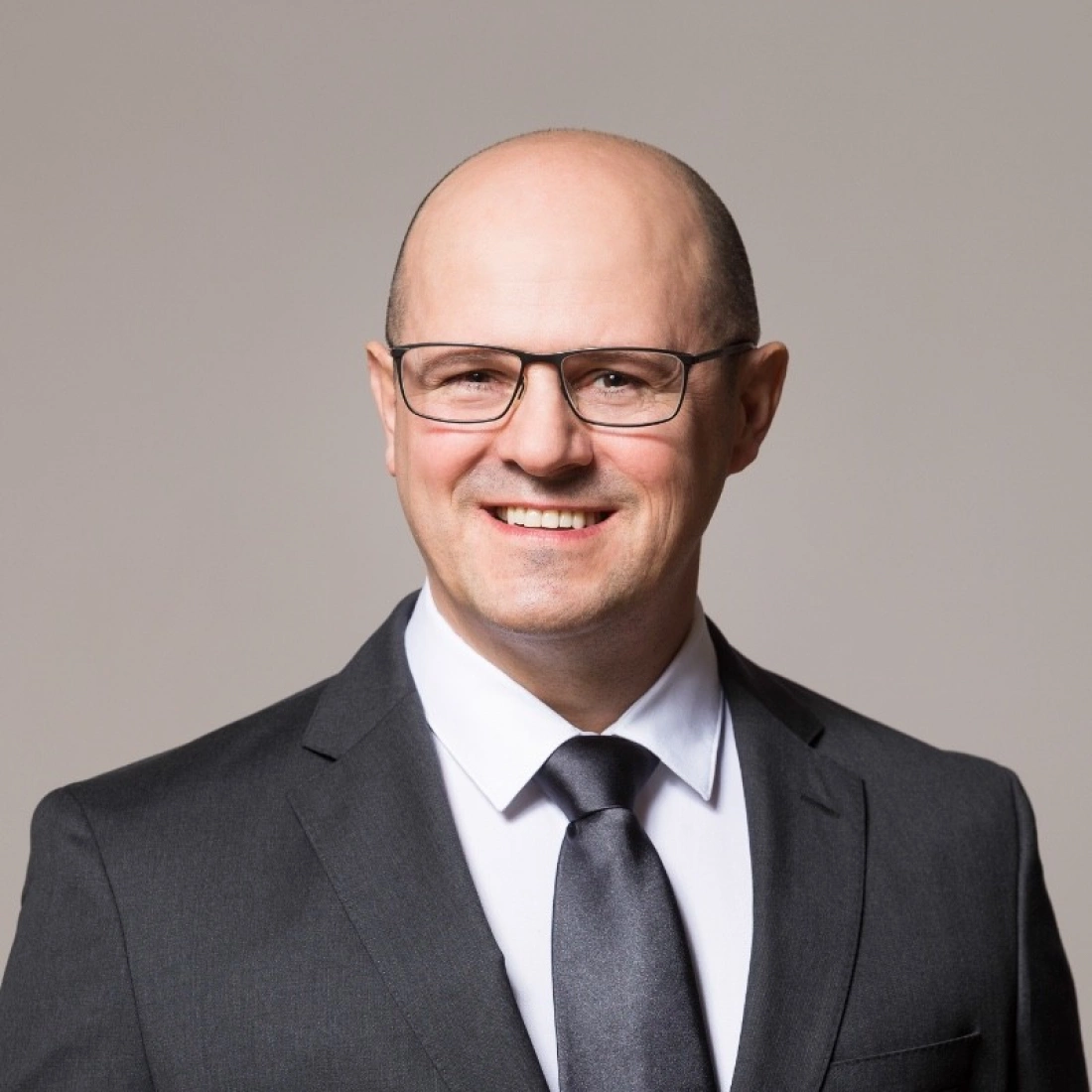 Mężczyzna w okularach, uśmiechający się, ubrany w garnitur.