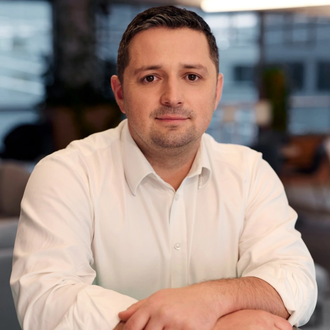 Mężczyzna w białej koszuli, siedzący przy biurku, z poważnym wyrazem twarzy.