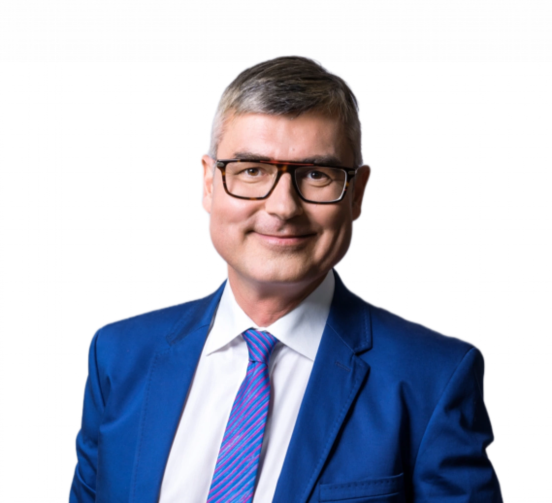 Mężczyzna w okularach, uśmiechający się w niebieskim garniturze z kolorowym krawatem.