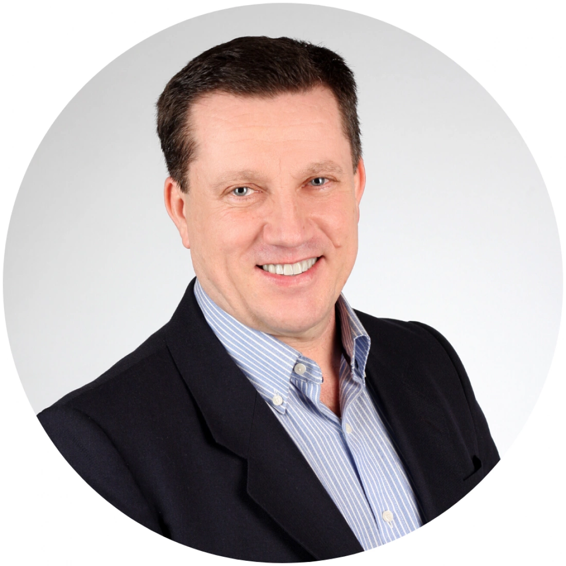 Mężczyzna z uśmiechem, w ciemnej marynarce i niebieskiej koszuli w paski, na jasnym tle.