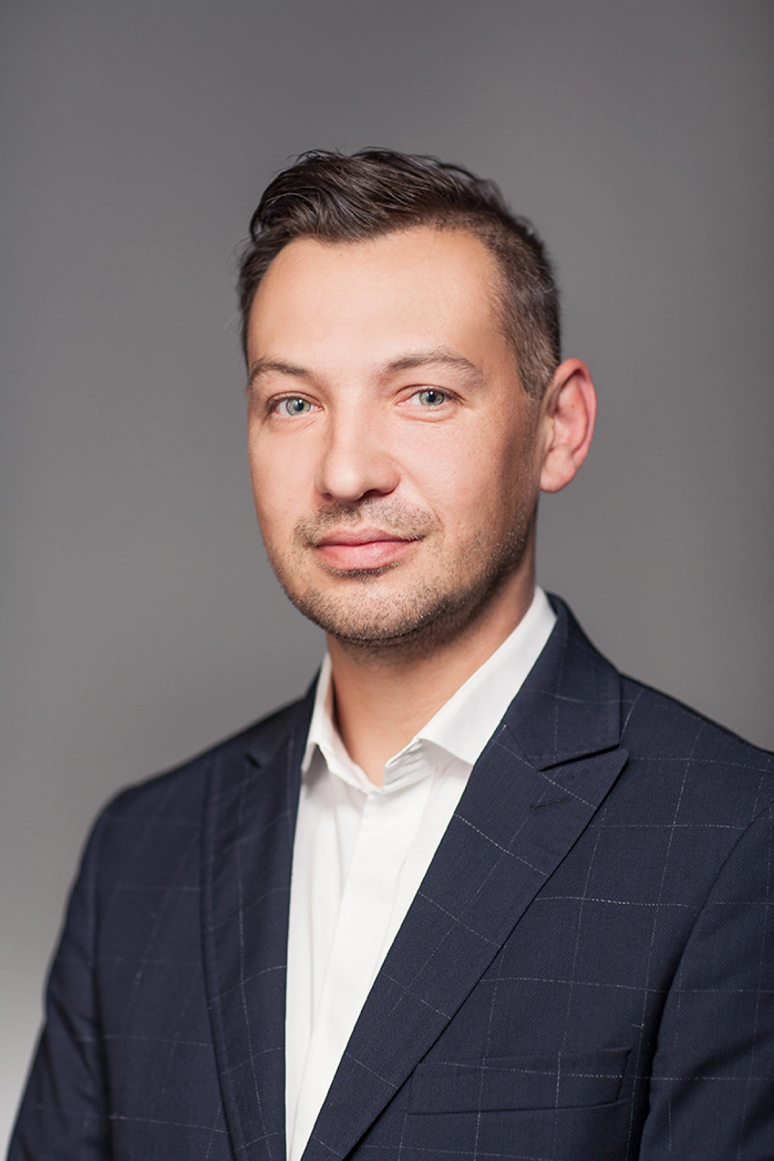 Mężczyzna w garniturze, z uśmiechem, na szarym tle.