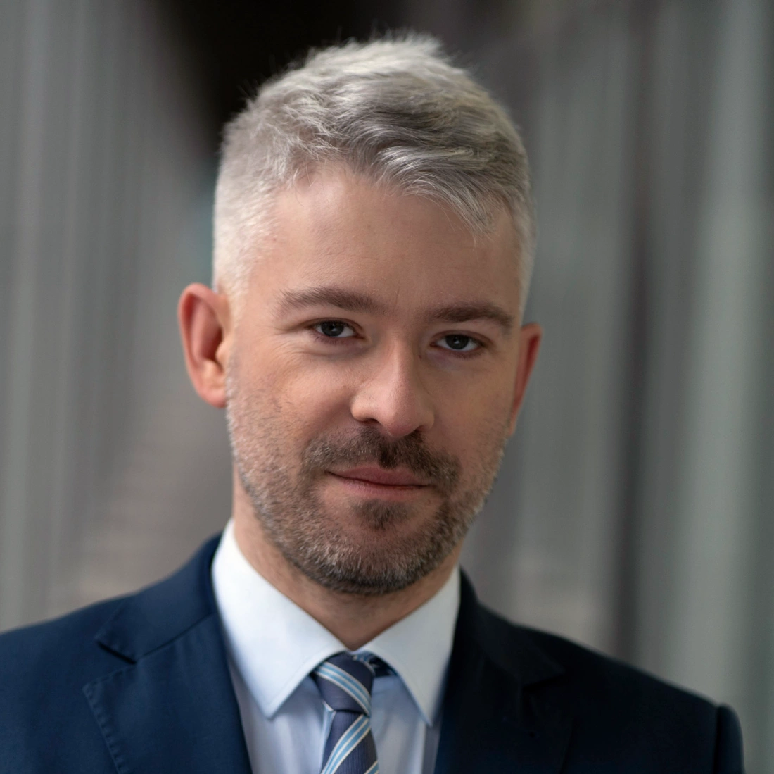 Mężczyzna w garniturze z jasnymi włosami, stojący w korytarzu.