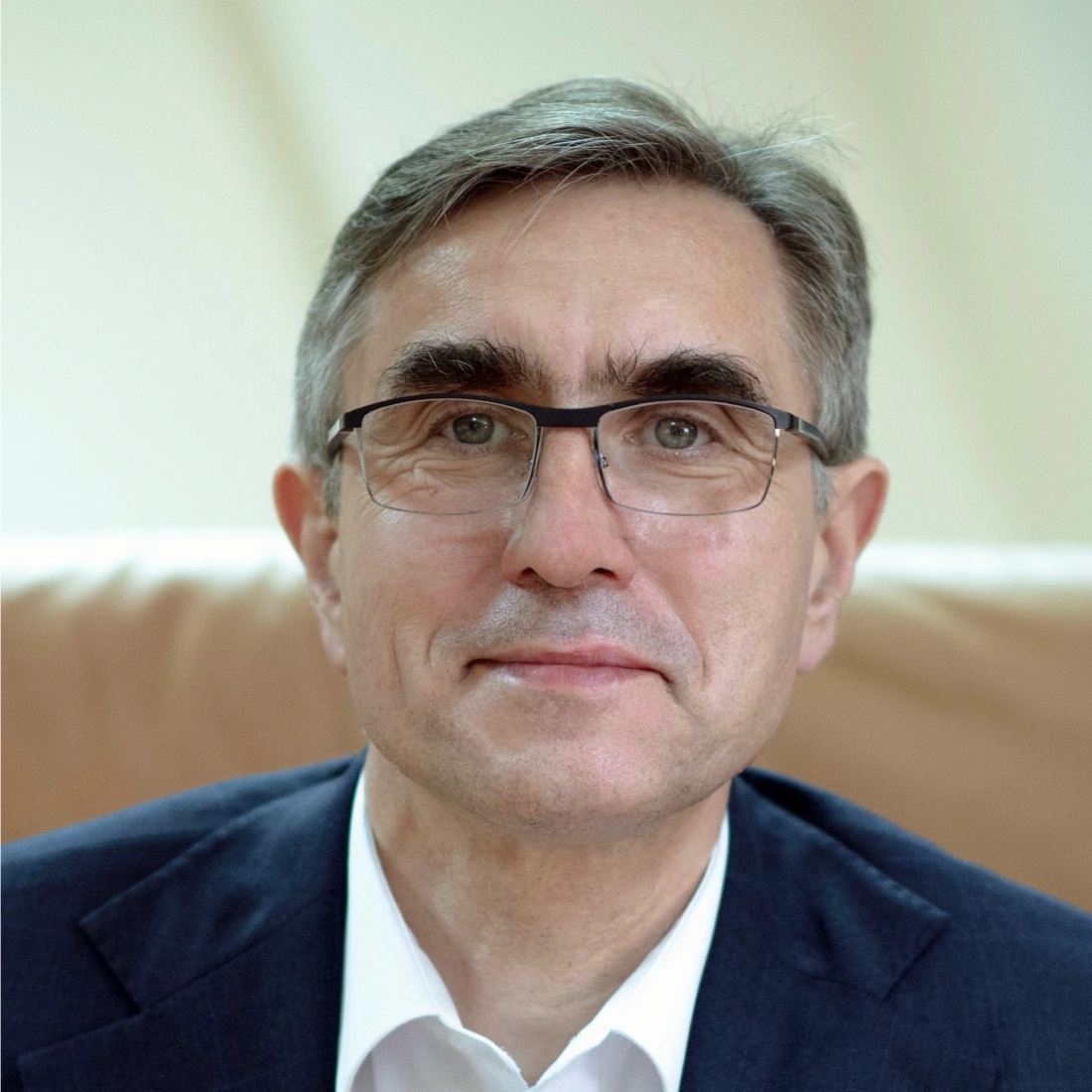 Mężczyzna w okularach, w garniturze, uśmiechający się.