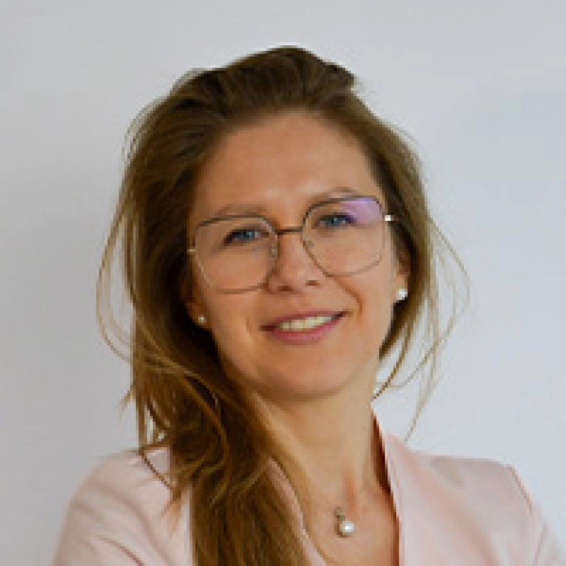 Młoda kobieta z długimi włosami, nosząca okulary, uśmiechająca się.