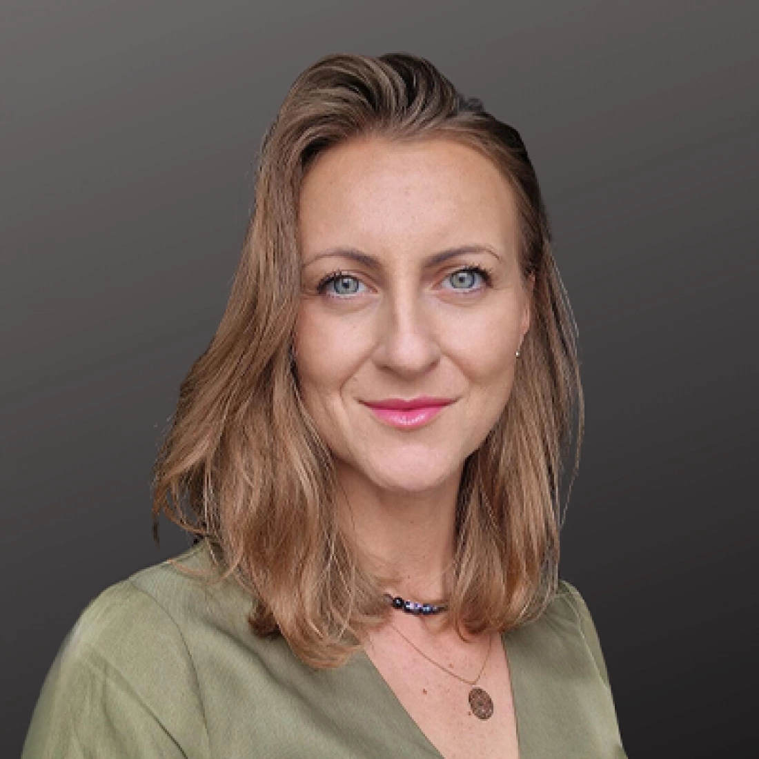 Kobieta z długimi, falującymi włosami, w oliwkowej bluzce, uśmiechająca się do kamery.