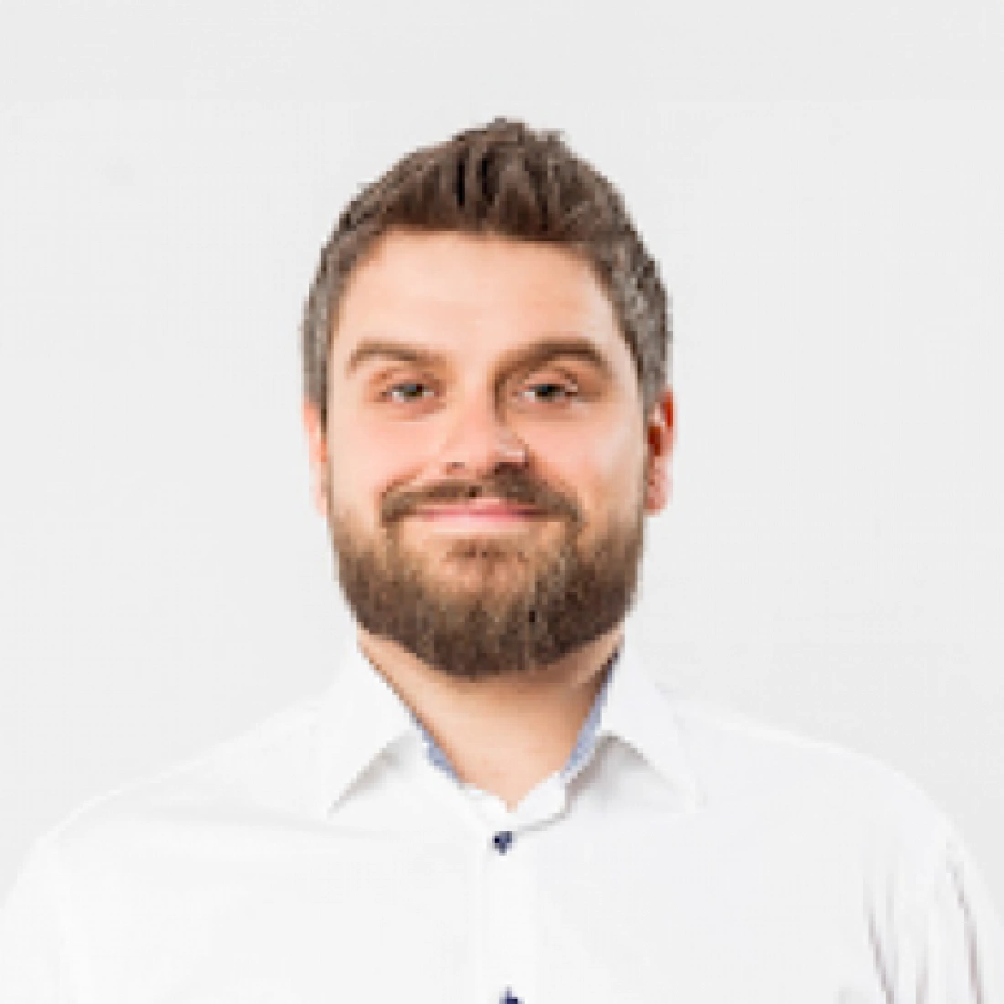 Mężczyzna w białej koszuli uśmiecha się na tle jednolitego tła.