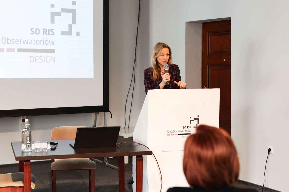 Prezentacja w trakcie wydarzenia dotyczącego projektowania, z mówczynią przy mównicy.