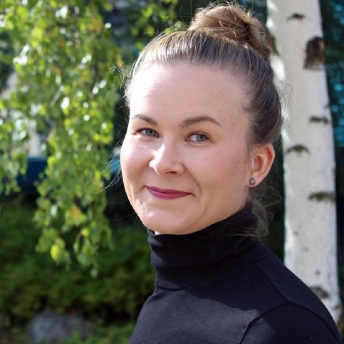 Młoda kobieta uśmiecha się, stojąc w plenerze w pobliżu drzew.