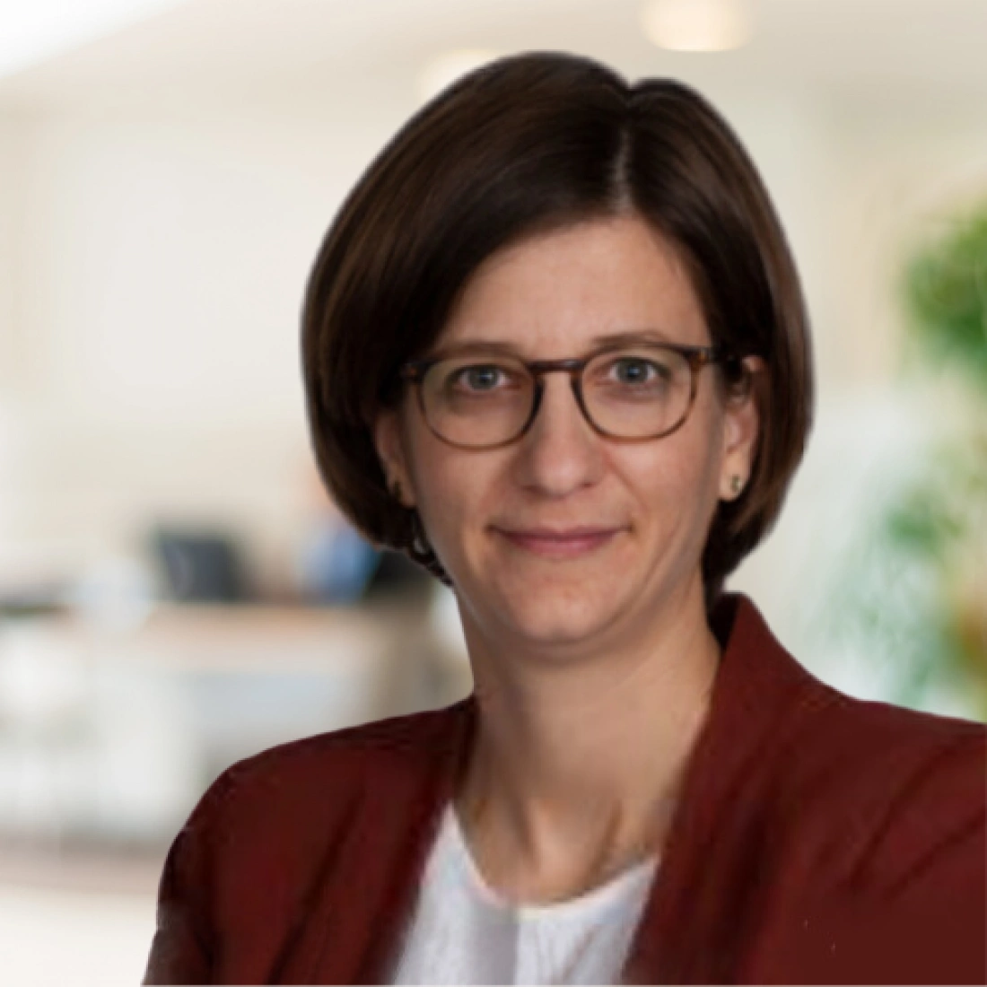 Kobieta w okularach, w jasnym wnętrzu biurowym, uśmiechająca się.