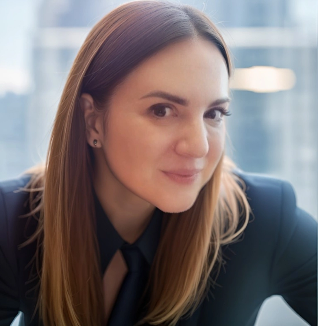 Kobieta z długimi włosami w garniturze, na tle okna biurowego.