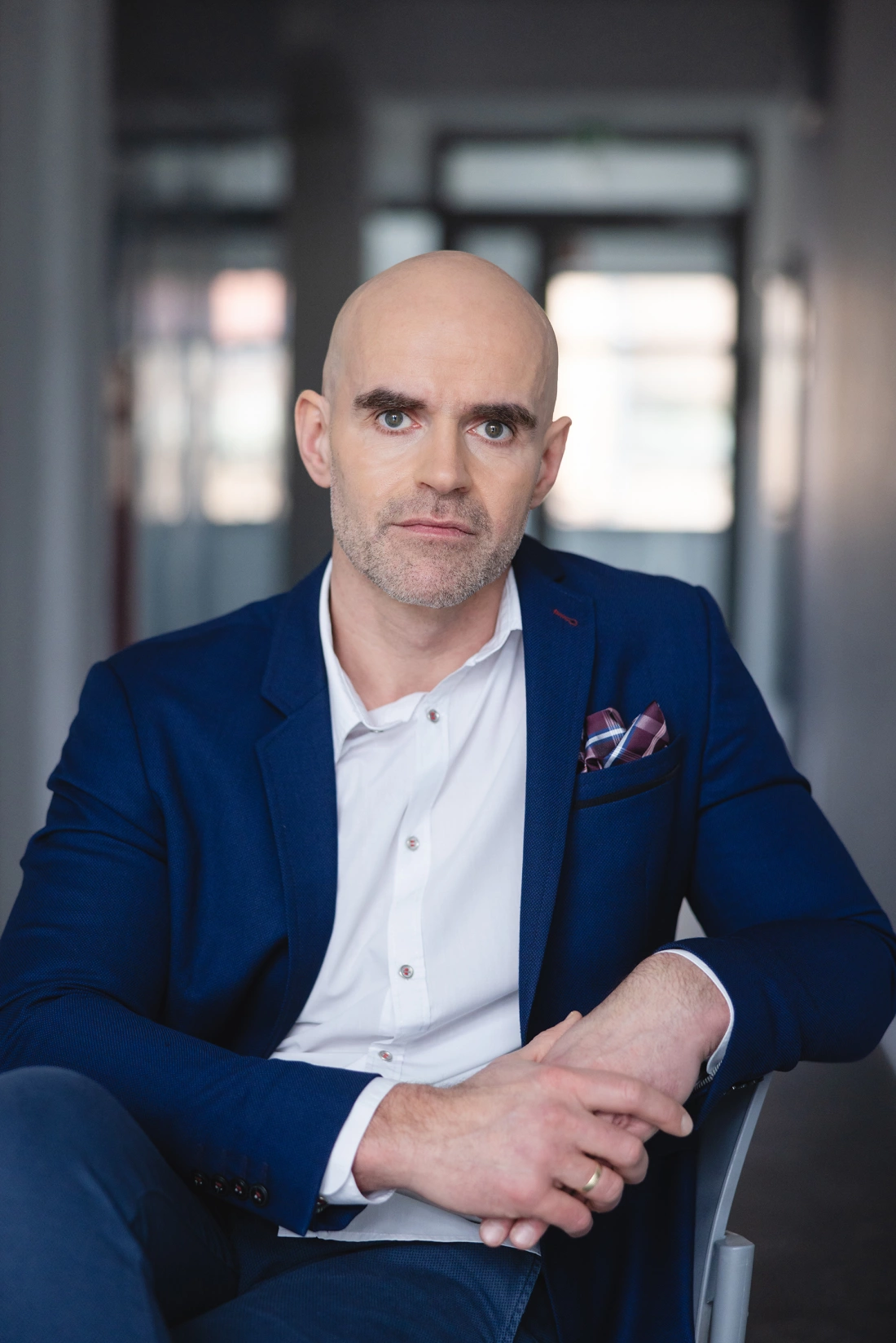 Mężczyzna w garniturze siedzi na krześle, patrząc prosto w obiektyw.