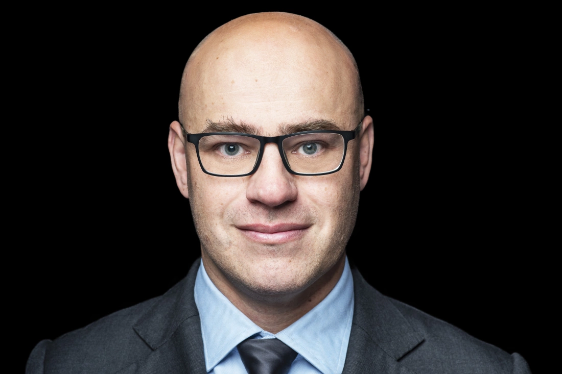 Mężczyzna w garniturze i okularach, z jasnym tłem.