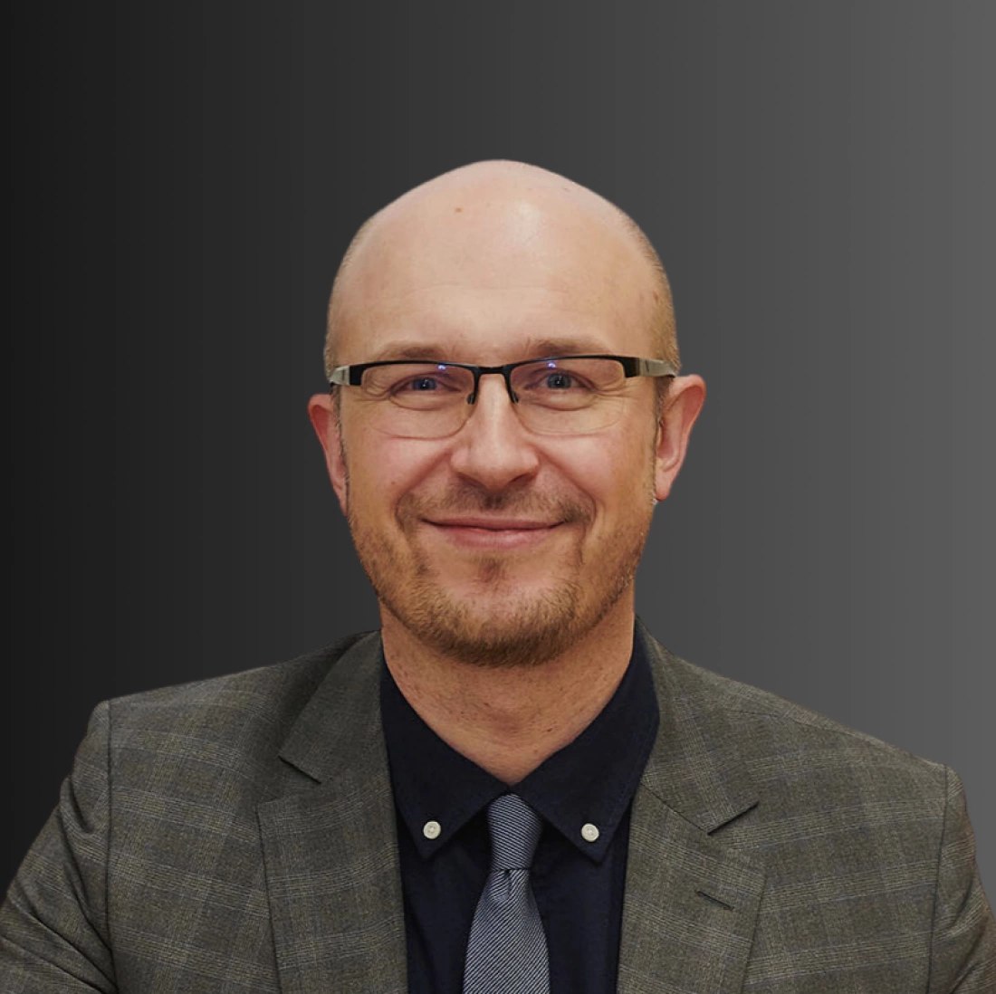 Mężczyzna w garniturze z okularami, uśmiechający się.